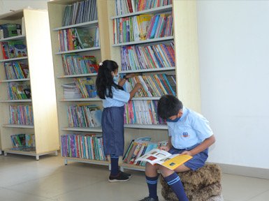 Bellwether children choosing and reading books by library shelves