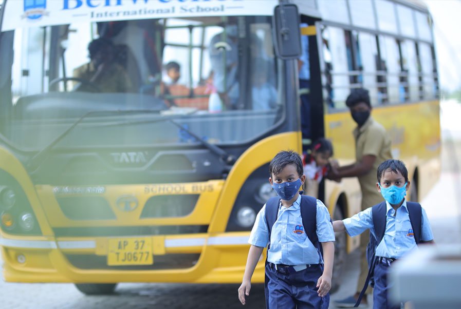 Bellwether students with school bags walking beside a yellow school bus